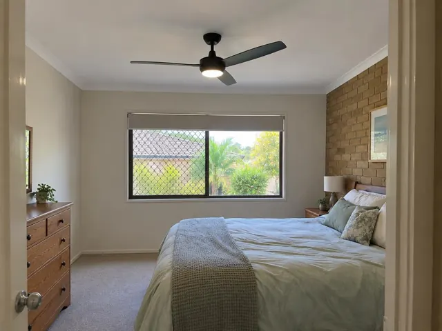 Bedroom with black ceiling fan above a bed, brick feature wall and window in Elanora