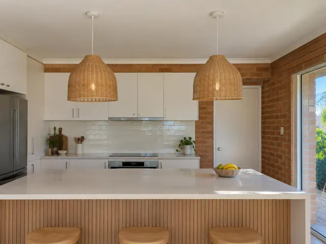 Two woven pendant lights over a white kitchen island in a brick-walled home in Palm Beach